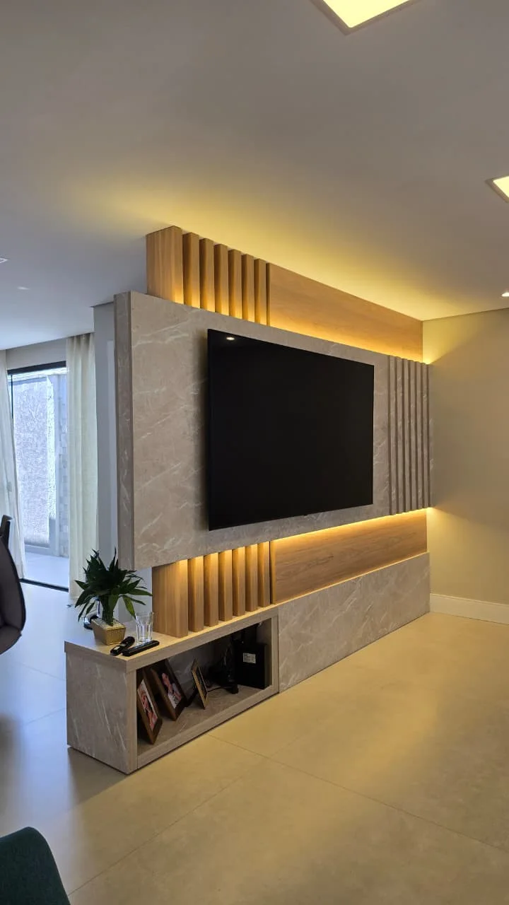 Painel de TV em porcelanato marmorizado com faixas de ripado em madeira e iluminação embutida em fita